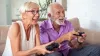 Two senior citizens on a couch, holding game controllers and looking happy