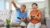Photograph of ageing man and women sitting on a couch and smiling while holding controllers
